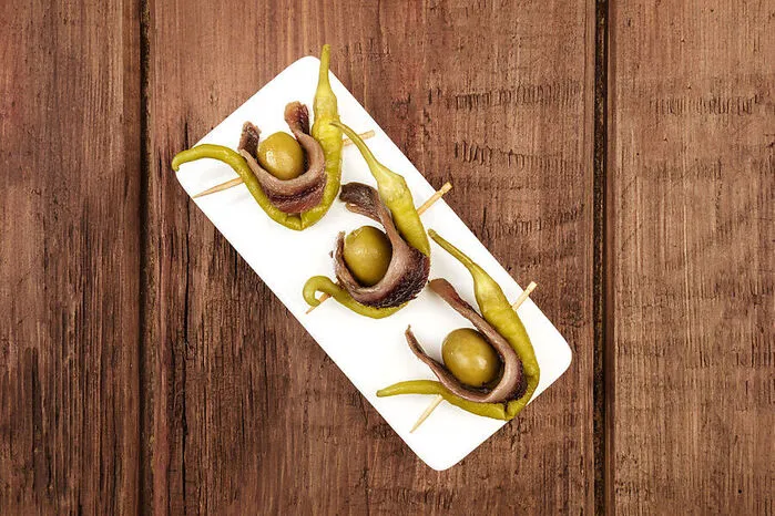 Zwei Oliven, zwei grüne Pfefferoni und ein Sardellenfilet – fertig ist „Gilda“. Der berühmteste unter den pintxos(baskische Tapas) wurde 1946 kreiert, als der gleichnamige Film mit Rita Hayworth in der Hauptrolle in den Kinos lief. Dazu: Txakoli-Wein.