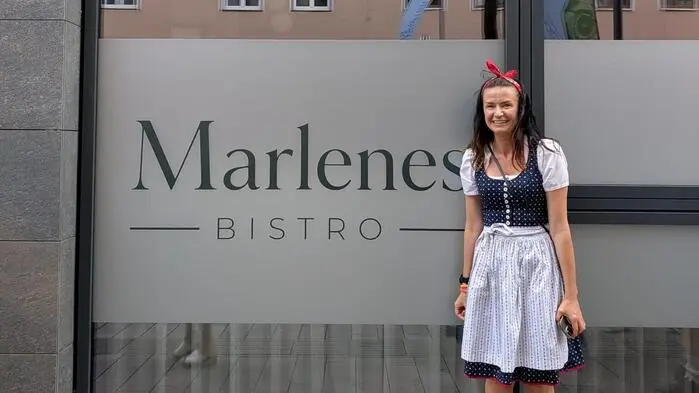 Eine junge Frau im Dirndl steht vor der Fensterfront eines Lokals