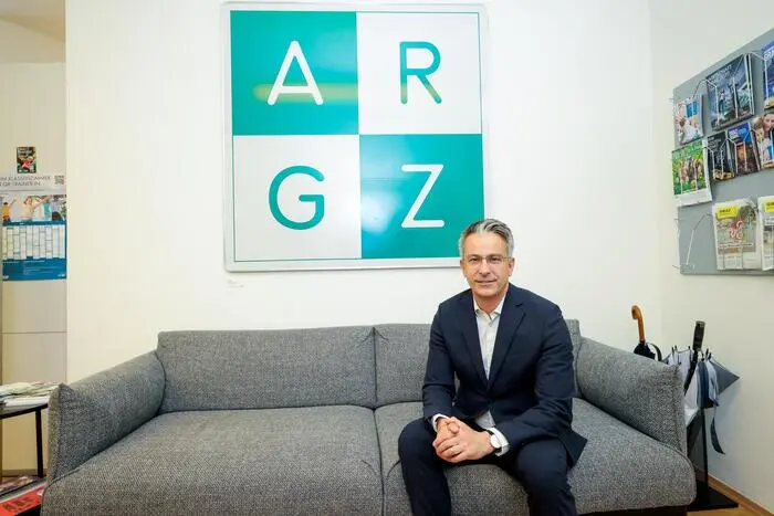 Kurt Hohensinner vor einem Kunstwerk von Peter Weibel in seinem Büro. Das Bild zeigt quadratisch die Buchstaben A und R und darunter G und Z
