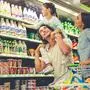 Beautiful young parents and their cute little daughter are smiling while choosing food in the supermarket. Girl is sitting on her dad's shoulders