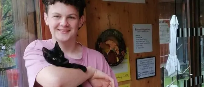 Ein Junge steht mit einer Katze am Arm vor dem Tierheim