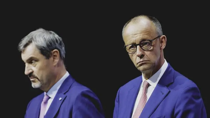 Markus Söder blickt nach links, Friedrich Merz nach rechts – beide tragen blaue Anzüge.