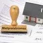 Mietvertrag und Modellhaus mit Mietpreisbremse Ein Stempel mit Aufdruck Mietpreisbremse steht auf einem Mietvertrag *** Tenancy agreement and model house with rent control A stamp with the imprint Mietpreisbremse is on a tenancy agreement