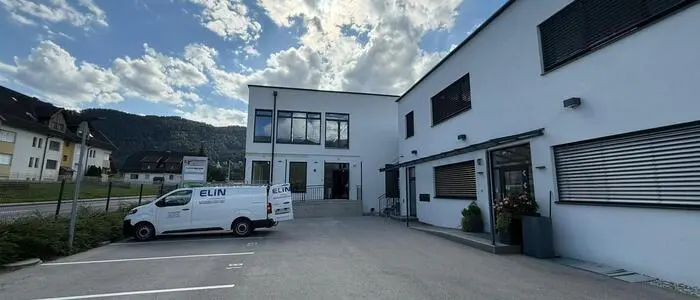 Ein weißes Industriegebäude, davor steht ein weißer Kastenwagen