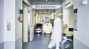 Notaufnahme Eingang Krankenhaus mit Arzt Rollstuhl und Patient in Bewegungsunschärfe auf dem Flur und Pfleger mit Krankenbett 