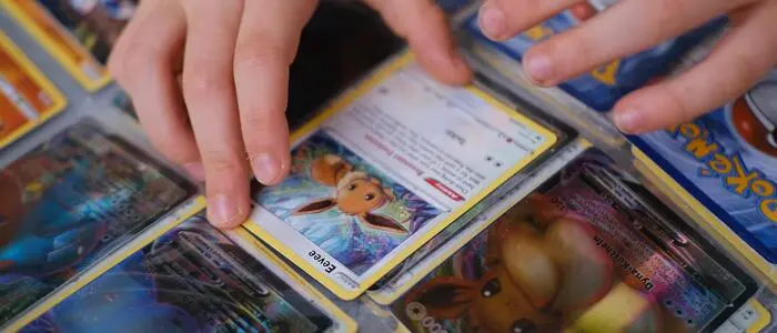 Eine Kinderhand greift zu einer Pokémon-Sammelkarte, die sich in einem Album befindet. | Seltene Pokémon-Sammelkarten können pro Stück mehrere tausend Euro wert sein (Symbolbild)