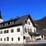 Ein uriges Gasthaus bei Sonnenschein. Im Hintergrund ist ein Kirchturm zu sehen.