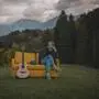 Musikerin mit Gitarre auf einer Couch, die im Grünen steht