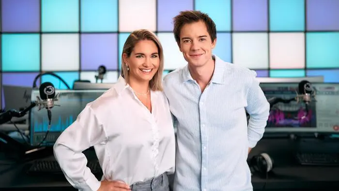 Ein Mann und eine Frau in einem Radio-Studio. Sie lächeln in die Kamera