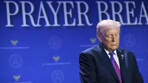 Das Bild zeigt US-Präsident Donald Trump mit geschlossenen Augen vor einem Hintergrund mit dem Schriftzug „Nationales Gebets-Frühstück“.