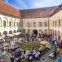 Auf dem Foto sieht man einen Blick in einen Arkadenhof mit Marktständen und einer Grüninsel in der Mitte. Zahlreiche Menschen schauen sich bei Sonnenschein die Geschenke und Produkte der Aussteller an | Der Ostermarkt im Arkadenhof des Schloss Retzhof lockt jährlich zahlreiche Besucher an