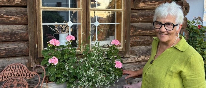 Eine Dame mit weißen Haaren und Brille steht neben einem Blumenstock