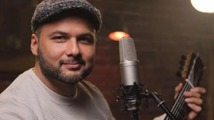 Ein Mann mit Kappe sitzt mit einer Gitarre vor einem Mikrofon