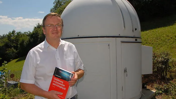 Arnold Hanslmeier vor seinem Privatobservatorium mit einem Standardwerk, das er verfasst hat
