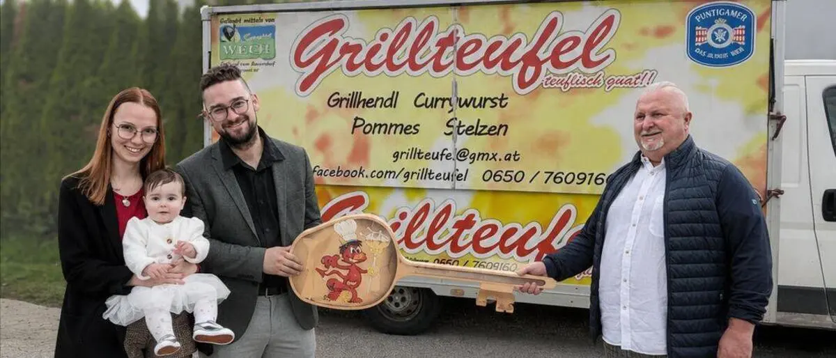 Eine Frau mit Baby in der Hand und zwei Männer stehen vor einem Foodtruck und überreichen sich einen symbolischen Schlüssel