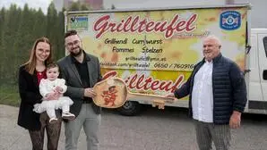 Eine Frau mit Baby in der Hand und zwei Männer stehen vor einem Foodtruck und überreichen sich einen symbolischen Schlüssel