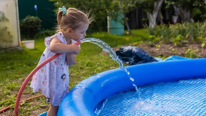 Zu sehen ist ein Mädchen, das aus einem Wasserschlauch trinkt 
