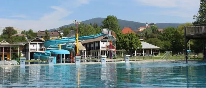 Ein Freibad, hinter dem Becken ist eine große blaue Wasserrutsche zu sehen.