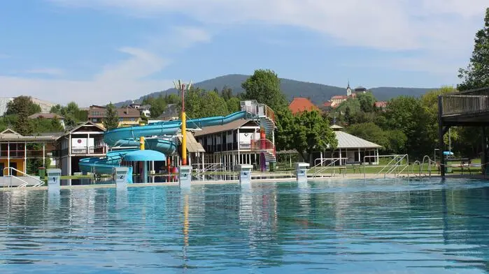 Ein Freibad, hinter dem Becken ist eine große blaue Wasserrutsche zu sehen.