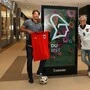 Zwei Männer stehen neben einer digitalen Anzeigetafel, einer trägt ein weißes Trikot der österreichischen Fußball-Nationalmannschaft, der andere hält ein rotes Trikot in seinen Händen.