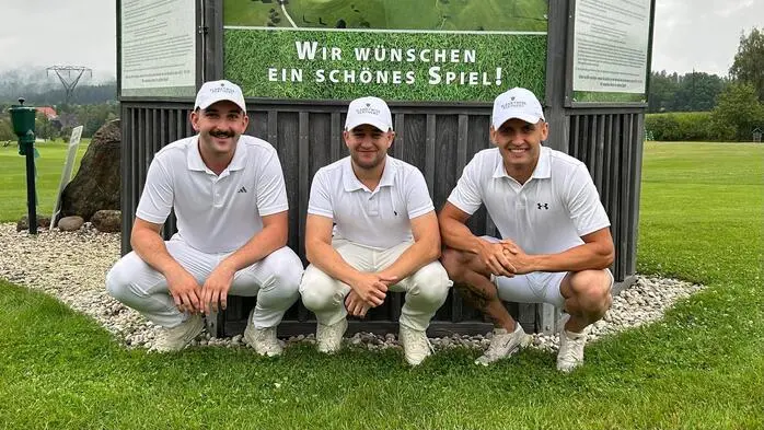 Drei Männer in einem weißen Outfit und mit weißen Kappen auf einem Golfplatz.