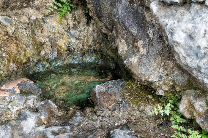 Dahinter entspringt aus einer Felswand die namensgebende Quelle: Wasser sammelt sich hier in kleinen, gemeißelten Steinschüsselchen – und diesem Wasser wird der Legende nach wundertätige Wirkung zugeschrieben.
