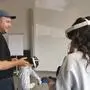 Ein Mann hält eine VR-Brille, rechts im Bild sieht man ein Mädchen von hinten, das eine VR-Brille trägt