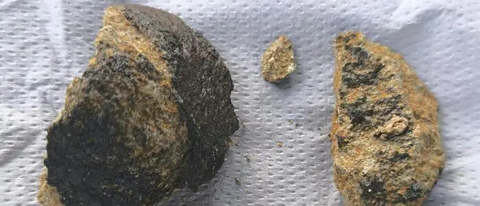 Meteoritenteile und ein Schlüsselbund liegen auf einem weißen Stück Papier.