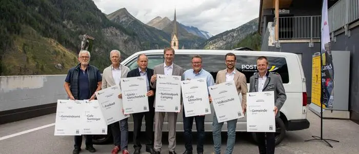 Sieben Männer vor einem Kleinbus und lachen in die Kamera
