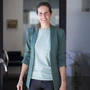 Eine Frau schaut im grün-blauen Blazer und blassem T-Shirt in die Kamera