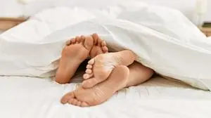 Couple feet under sheets on the bed at home.