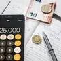 Ein Taschenrechner, ein Stift und Geld liegen auf einem Kalender