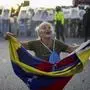 Consuelo Marquez holds a Venezuelan flag in front of police blocking demonstrations against the official election results declaring President Nicolas Maduro's reelection, the day after the vote in Caracas, Venezuela, Monday, July 29, 2024. (AP Photo/Matias Delacroix)