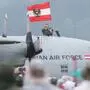 Flugzeug der Austrian Air Force. Aus einer Luke ragt eine Person in Militäruniform und mit einer Österreich-Fahne in der Hand. Davor steht ein Publikum.