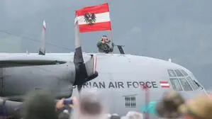 Flugzeug der Austrian Air Force. Aus einer Luke ragt eine Person in Militäruniform und mit einer Österreich-Fahne in der Hand. Davor steht ein Publikum.