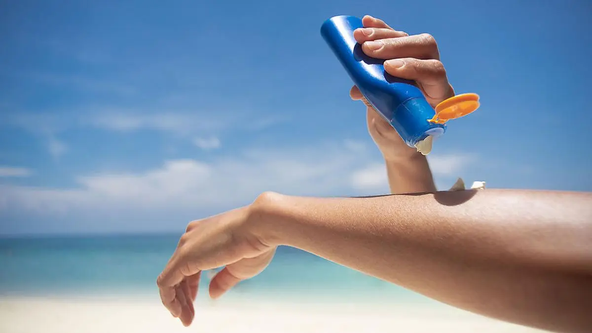 Woman applying sunscreen on her hands from a bottle on the beach with the sea in the background. SPF sunblock protection concept.selective focus