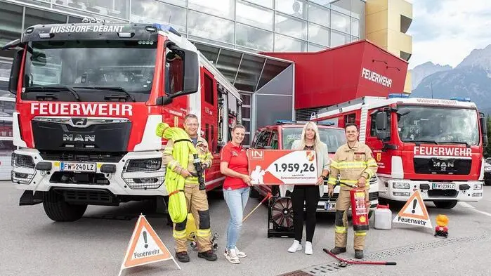 Zwei Frauen übergeben einen Scheck an zwei Feuerwehrmitglieder, im Hintergrund sind zwei Feuerwehrautos