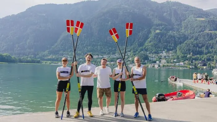 Mehrere Ruderinnen und Ruderer stehen mit Paddeln vor einem See