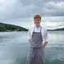 Ein junger Erwachsener steht in Kochkleidung vor einem See