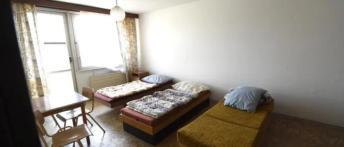 Ein enges Zimmer für Asylwerber, drei Einzelbetten nebeneinander aufgereiht, davor ein Tisch mit drei Sesseln