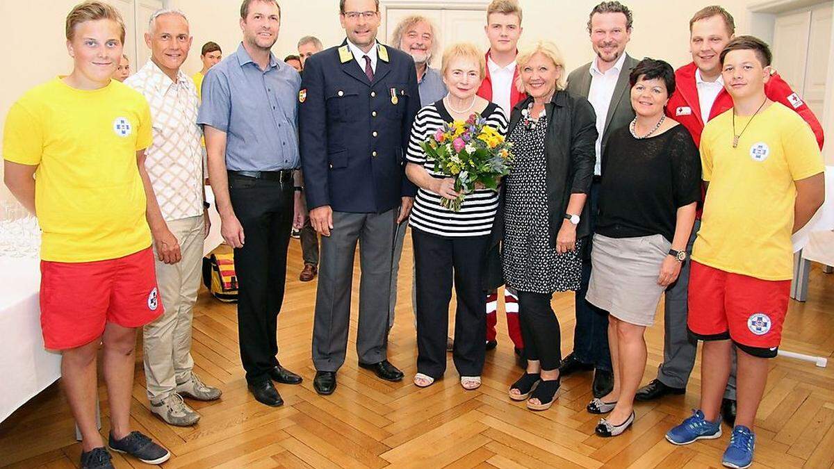 Friederike Raab (mit Blumenstrauß) wurde von Mario Moritz (links neben ihr) gerettet. Dazu gratulierte Bürgermeisterin Maria-Luise Mathiaschitz im Beisein zahlreicher Senatskollegen und dem Roten Kreuz mit Bezirksstellenleiter Philip Kucher und Sanitäter Matthias Kopitar recht herzlich.