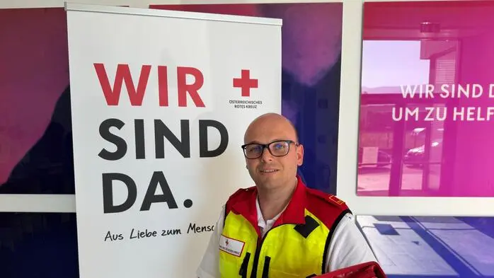 Ein Mann in Uniform hält eine rote Mappe, vor einem Aufsteller