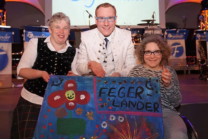 Was diesen Abend aber auszeichnete, waren seine Ehrengäste: Beeinträchtigte Menschen, die von der Initiative Monel betreut werden, durften die Musiker in den ersten Reihen hautnah miterleben. Sabine Ebner, die im Rollstuhl sitzt, schenkte ihrer Lieblingsband ein selbst gemaltes Bild. Am Foto: Monika Wegscheider, Walter Grechenig, Sabine Ebner