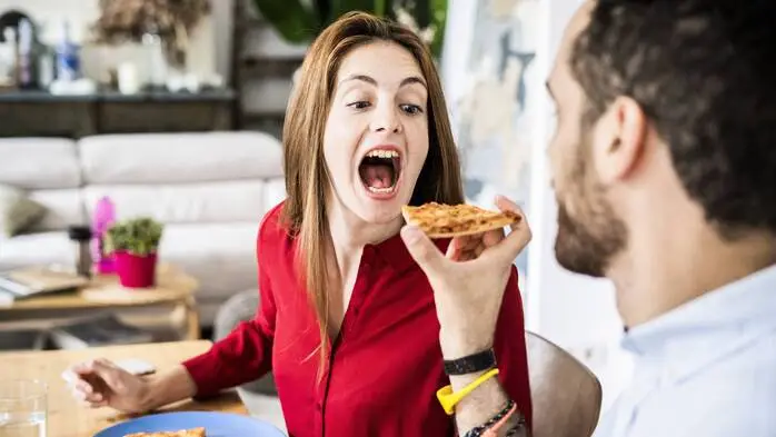Ein Mann füttert eine Frau mit einem Stück Pizza.