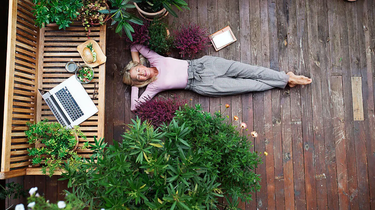 Top view of senior woman with laptop lying outdoors on terrace, resting.