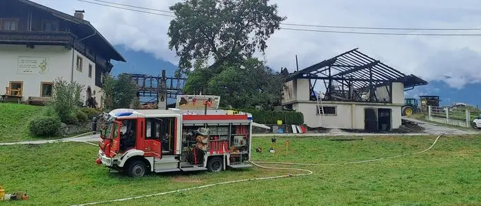 Ein Feuerwehrauto und im Hintergrund eine Brandruine eines Wirtschaftsgebäudes