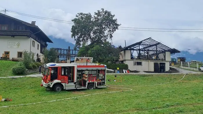 Ein Feuerwehrauto und im Hintergrund eine Brandruine eines Wirtschaftsgebäudes