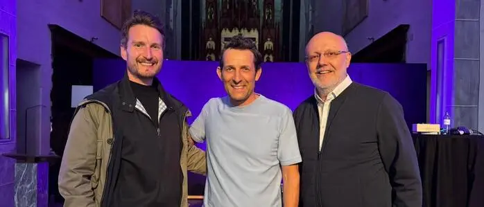 Drei Männer lachen in die Kamera, sie stehen in einer Domkirche