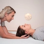 Eine Frau mit blonden Haaren hält eine Patientin am Kopf 