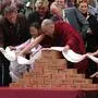 Der Dalai Lama beugt sich über mehrere Backsteine 